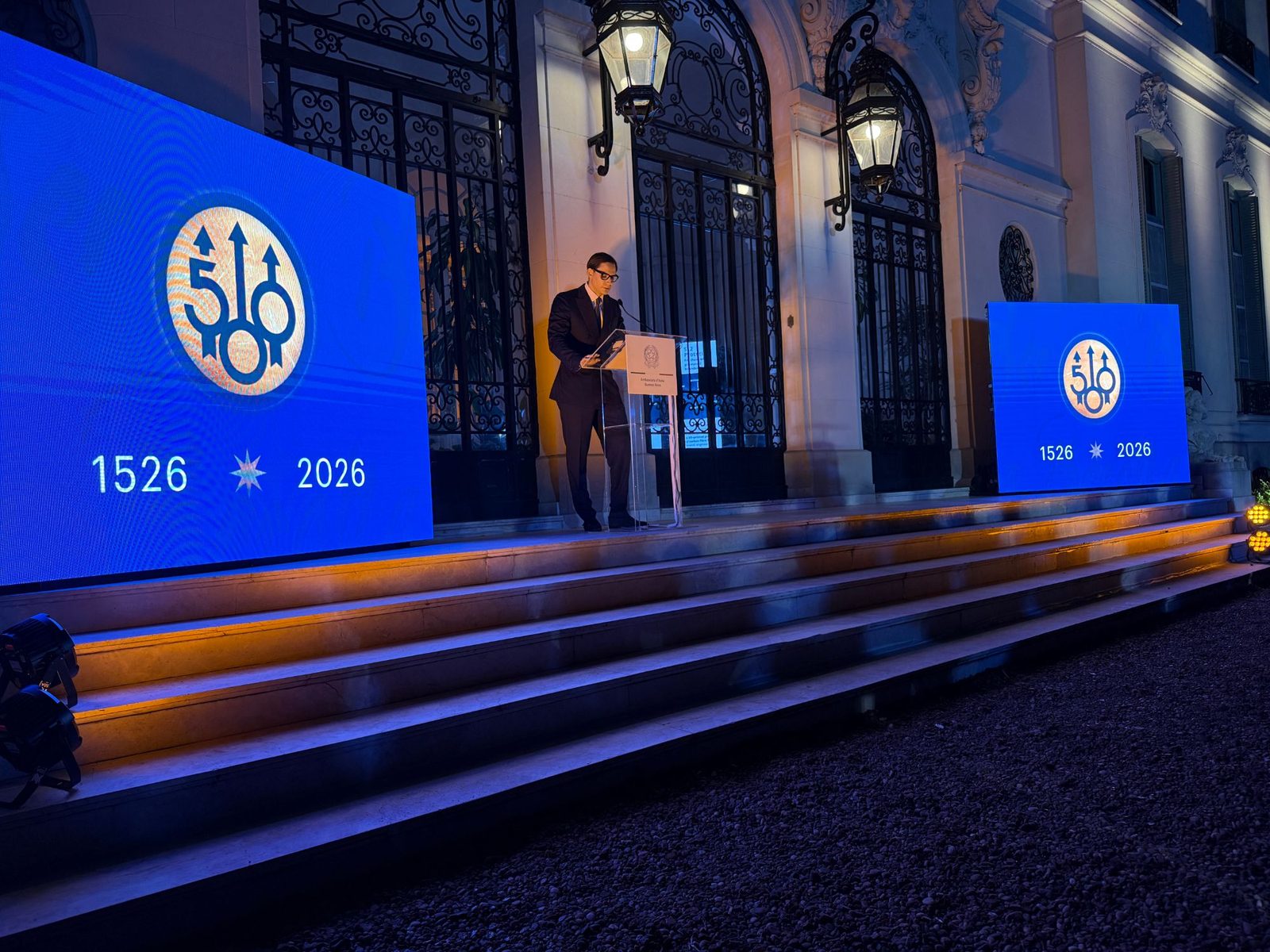 A speaker at the Embassy of Italy lectern, between screens marking Beretta’s 500 years